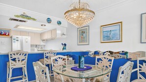 A dining area with a glass table surrounded by intricately carved wicker chairs, a chandelier, and framed artwork on the walls. - Gulfstream Condos Unit 511 | Gulf-Front Balcony | Pool & Hot Tub (Corpus Christi)