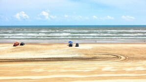 A beach with vehicles and a tent. - GSC Unit 512 | Pickleball, Pool, Hot Tub & BBQ | Beachfront View (Corpus Christi)