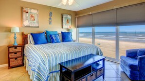 Une chambre dotée d’un grand lit, d’un ventilateur de plafond, d’une vue sur la plage et d’une fenêtre avec des stores.