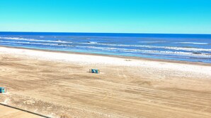 Une plage avec un ciel dégagé, un rivage sablonneux et une petite construction visible au loin.
