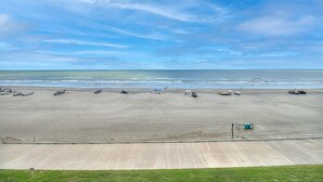 Ein weiter Sandstrand, ein klarer Himmel, einige geparkte Autos und eine kleine Bebauung in der Ferne.