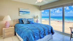 A bedroom with a bed, nightstands, a ceiling fan, and a large window offering a beach view. - Gulfstream Condos Unit 516 | Gulf-Front Balcony | Pool & Hot Tub (Corpus Christi)