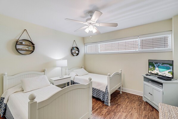 A bedroom with two single beds, a ceiling fan, a TV, and a window with blinds. - Gulfstream Condos Unit 517 | Beachfront with Panoramic Views | Pool, Hot Tub (Corpus Christi)