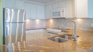 A modern kitchen with white cabinets, a stainless steel refrigerator, a microwave, a gas stove, and a granite countertop. - Gulfstream Condos Unit 521| Gulf-View Balcony | Heated Pool, Hot Tub (Corpus Christi)