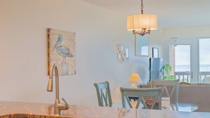 A kitchen with a sink, a dining area with chairs, a table, and a view of the ocean. - Gulfstream Condos Unit 521| Gulf-View Balcony | Heated Pool, Hot Tub (Corpus Christi)