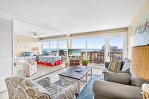 A spacious living room with a large window, a ceiling fan, a television, and a view of the ocean. - Gulfstream Condos Unit 522 | Gulf-View Balcony | Heated Pool, Hot Tub (Corpus Christi)