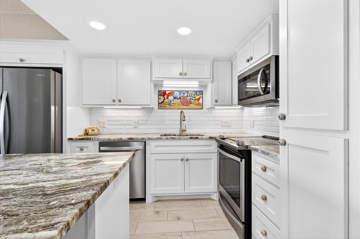 A kitchen with white cabinetry, a stainless steel refrigerator, a microwave, and a sink.