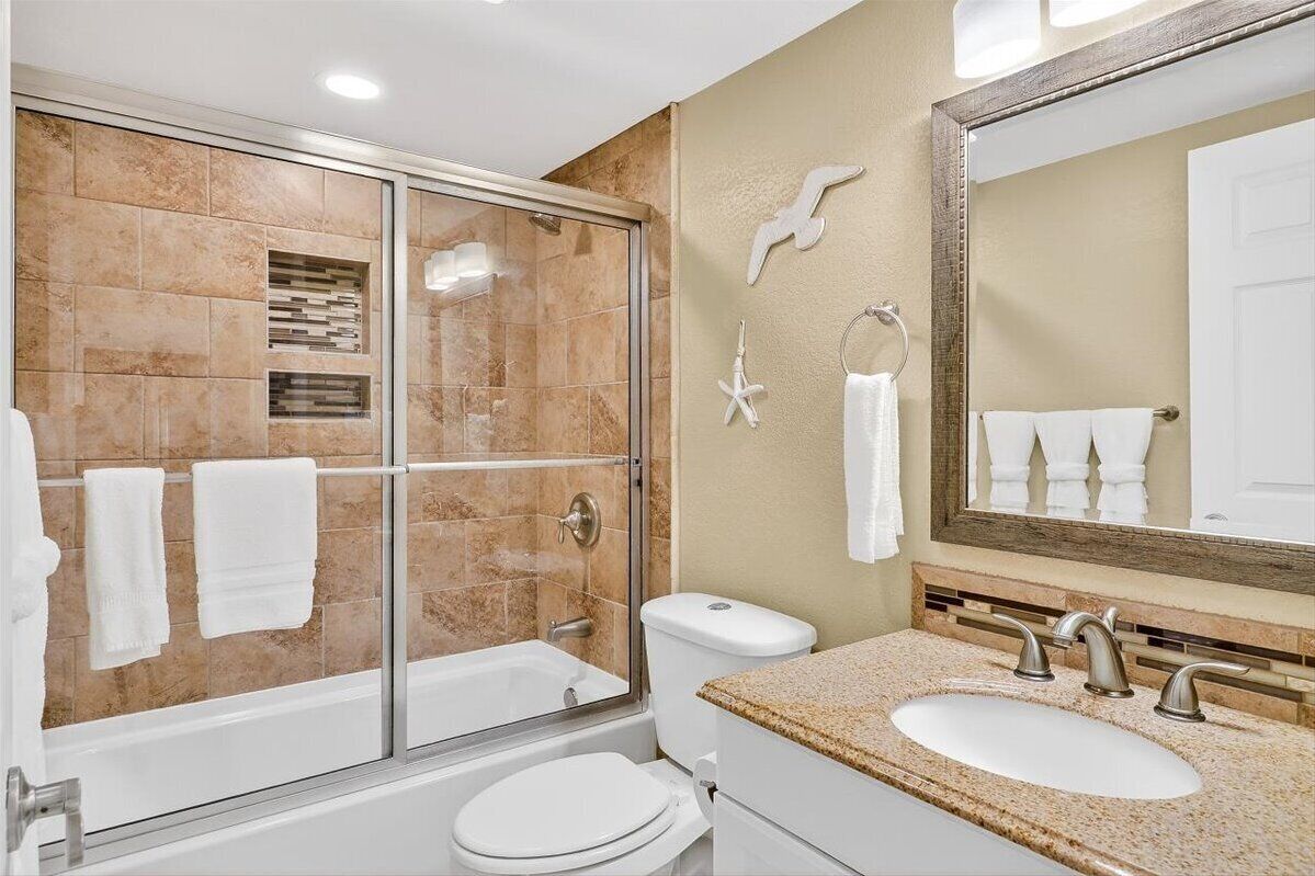 A bathroom with a glass-enclosed shower, a toilet, a sink with a mirror, and decorative wall tiles.