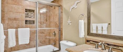 A bathroom with a glass-enclosed shower, a toilet, a sink with a mirror, and decorative wall tiles.