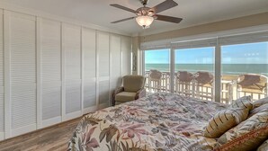 Ein Schlafzimmer mit einem großen Bett, einem Deckenventilator und Blick auf den Strand durch große Fenster.