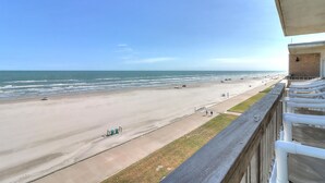 Blick auf einen Strand vom Balkon aus, mit blauem Himmel, Sandstrand und einigen Spaziergängern.