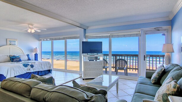 A room with a bed, a sofa, a TV, and a balcony with a view of the beach. - Gulfstream Condos Double Unit | 2 Adjoining Beachfront Top-Floor Units (Corpus Christi)