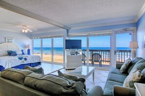 A room with a bed, a sofa, a TV, and a balcony with a view of the beach. - Gulfstream Condos Double Unit | 2 Adjoining Beachfront Top-Floor Units (Corpus Christi)