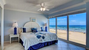 A bedroom with a large window overlooking a beach, a ceiling fan, and a bed with floral bedding. - Gulfstream Condos Double Unit | 2 Adjoining Beachfront Top-Floor Units (Corpus Christi)