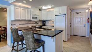 A kitchen with white cabinets, a black countertop, and two wicker bar stools. - Gulfstream Condos Double Unit | 2 Adjoining Beachfront Top-Floor Units (Corpus Christi)