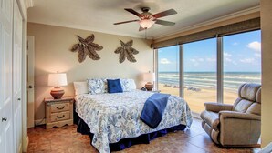 A bedroom with a bed, two nightstands, a ceiling fan, and a large window with a beach view. - Gulfstream Condos Unit 616 | Top-Floor | Gulf Front Views (Corpus Christi)