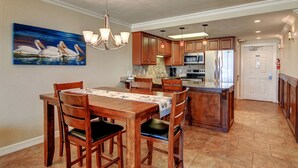A spacious kitchen with wooden cabinets, a central island, and a dining area with a table and chairs. - Gulfstream Condos Unit 616 | Top-Floor | Gulf Front Views (Corpus Christi)