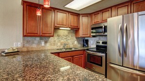 A kitchen with granite countertops, wooden cabinets, stainless steel appliances, and pendant lighting. - Gulfstream Condos Unit 616 | Top-Floor | Gulf Front Views (Corpus Christi)