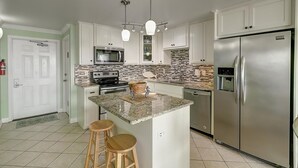 Una cocina moderna con armarios blancos, un refrigerador de acero inoxidable, un microondas y una estufa. Hay dos taburetes de madera en la isla.