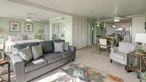 Amplia sala de estar con un sofá gris, comedor con mesa y sillas de madera, cocina con electrodomésticos modernos y un espejo grande que refleja la habitación.