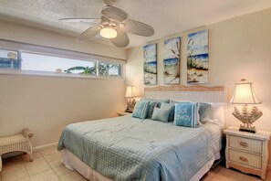Un dormitorio con una cama grande, un ventilador de techo, una ventana con vistas y obras de arte en la pared.