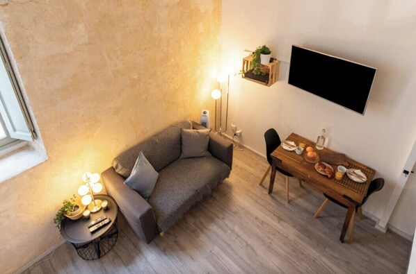 A cozy living area with a sofa, a dining table set with food, a TV mounted on the wall, and a lamp on a side table.