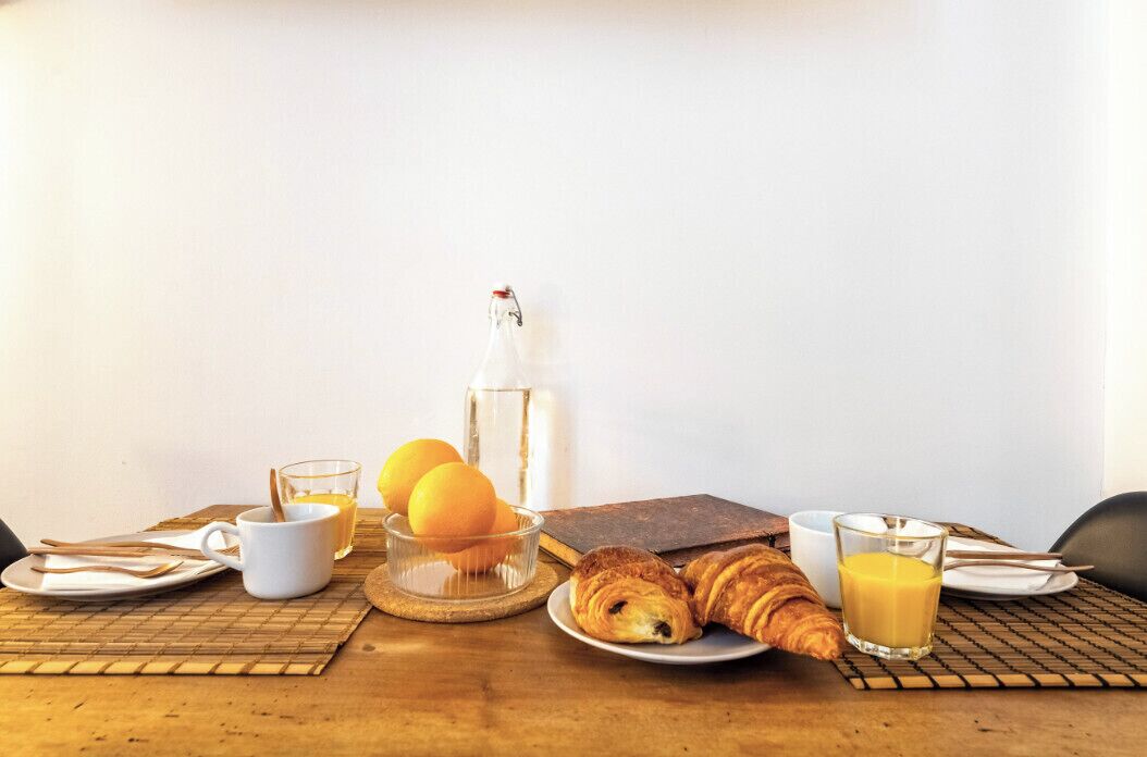 Een ontbijttafel met croissants, sinaasappelsap, een fles water en een glas sinaasappelsap.