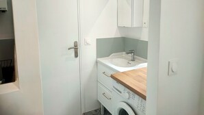 Une petite salle de bain avec une porte blanche, un lavabo doté d’un plan de travail en bois, un miroir au-dessus du lavabo et un lave-linge.
