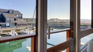 A view from a balcony overlooking a marina with boats, a bridge, and buildings in the background. - Sublime apartment facing the Port & Planches (Deauville)