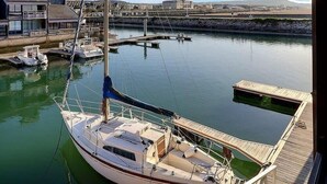 A sailboat docked at a marina with a view of a building and calm water. - Sublime apartment facing the Port & Planches (Deauville)