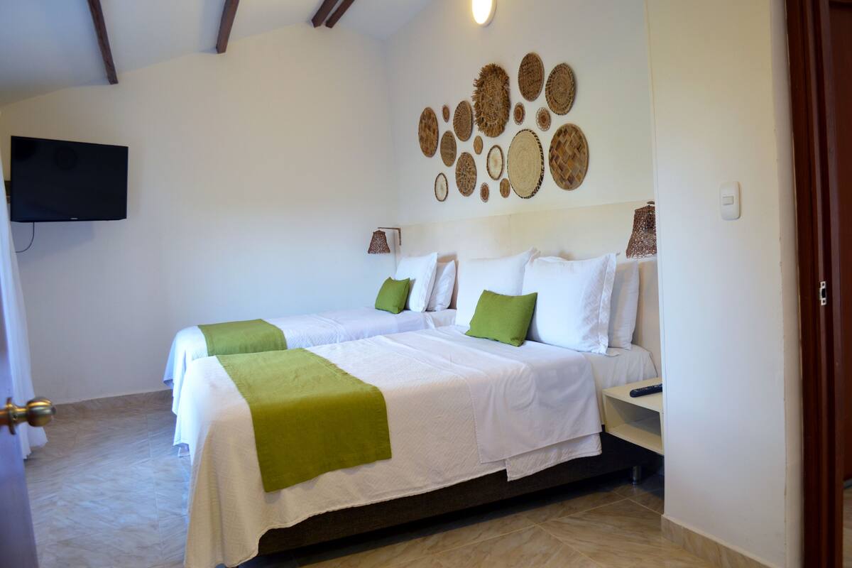 Une chambre d’hôtel avec deux lits, un téléviseur à écran plat et un mur décoré d’œuvres d’art tissées.