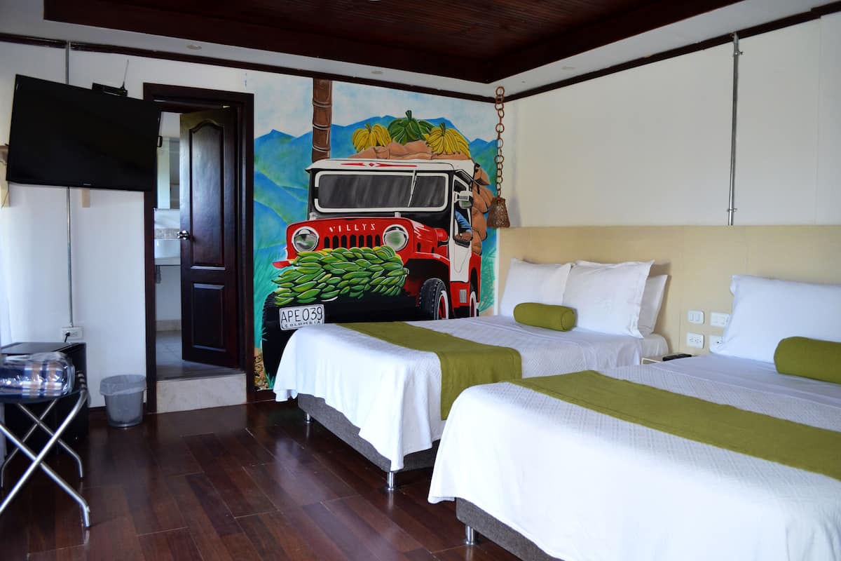 Une chambre d’hôtel avec deux lits, une fresque représentant un camion rouge et un téléviseur fixé au mur.
