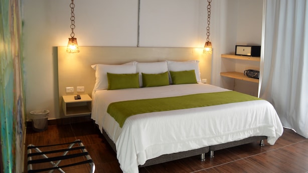 Una cama bien hecha con ropa de cama blanca y verde, una mesita de noche con lámpara y una estantería con radio.