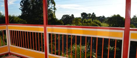 Un balcón con barandillas amarillas y rojas, con vistas a un paisaje verde exuberante con árboles y un cielo despejado.