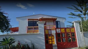 Un edificio de dos pisos con un portón rojo y amarillo, paredes blancas y techo de tejas.