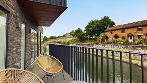 A balcony with wicker chairs and a table, overlooking a canal with buildings and graffiti in the background. - Be London - The St Pancras Residences (London)