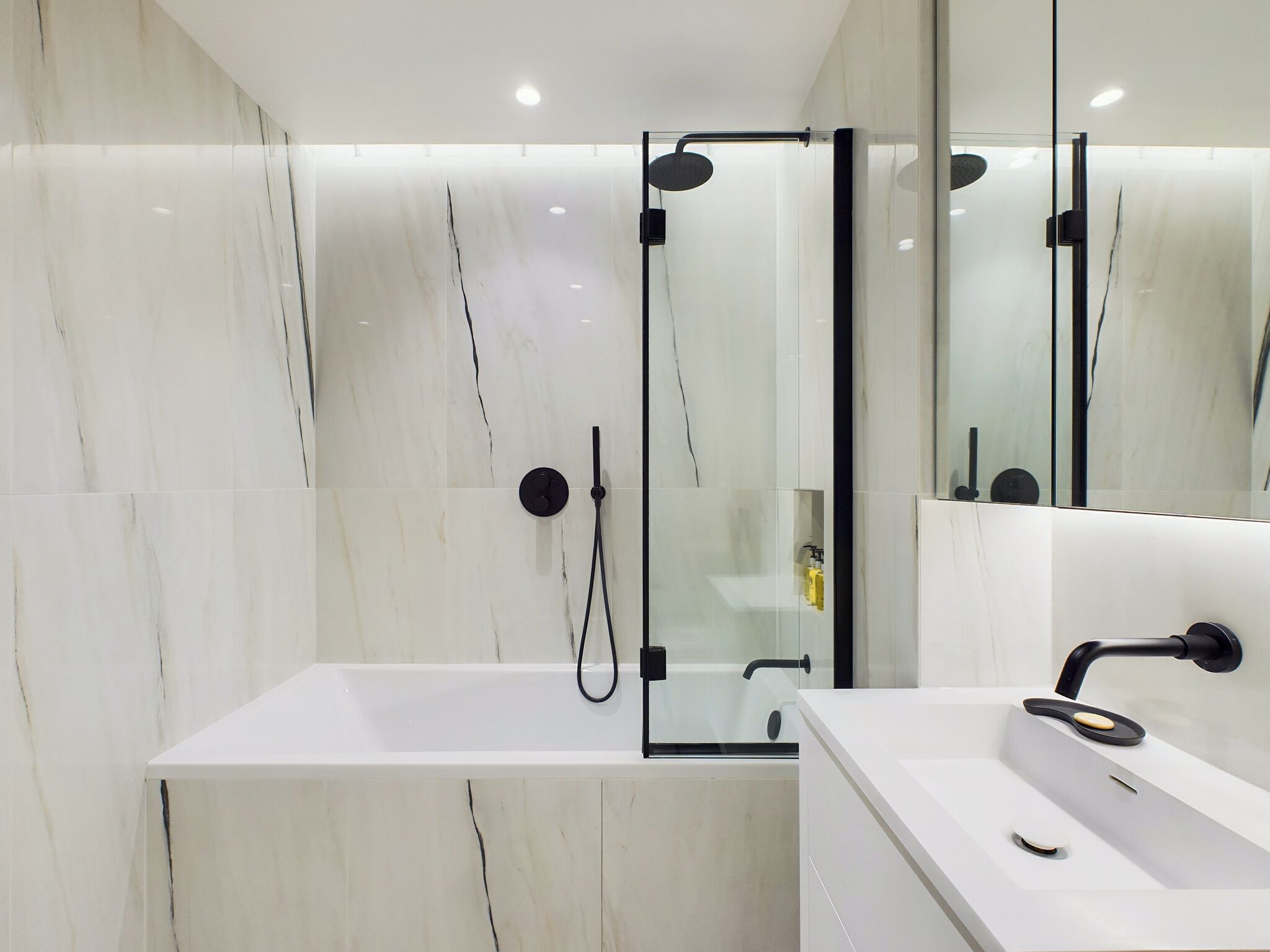 A modern bathroom with a glass-enclosed shower, a white bathtub, and a sink with a black faucet.