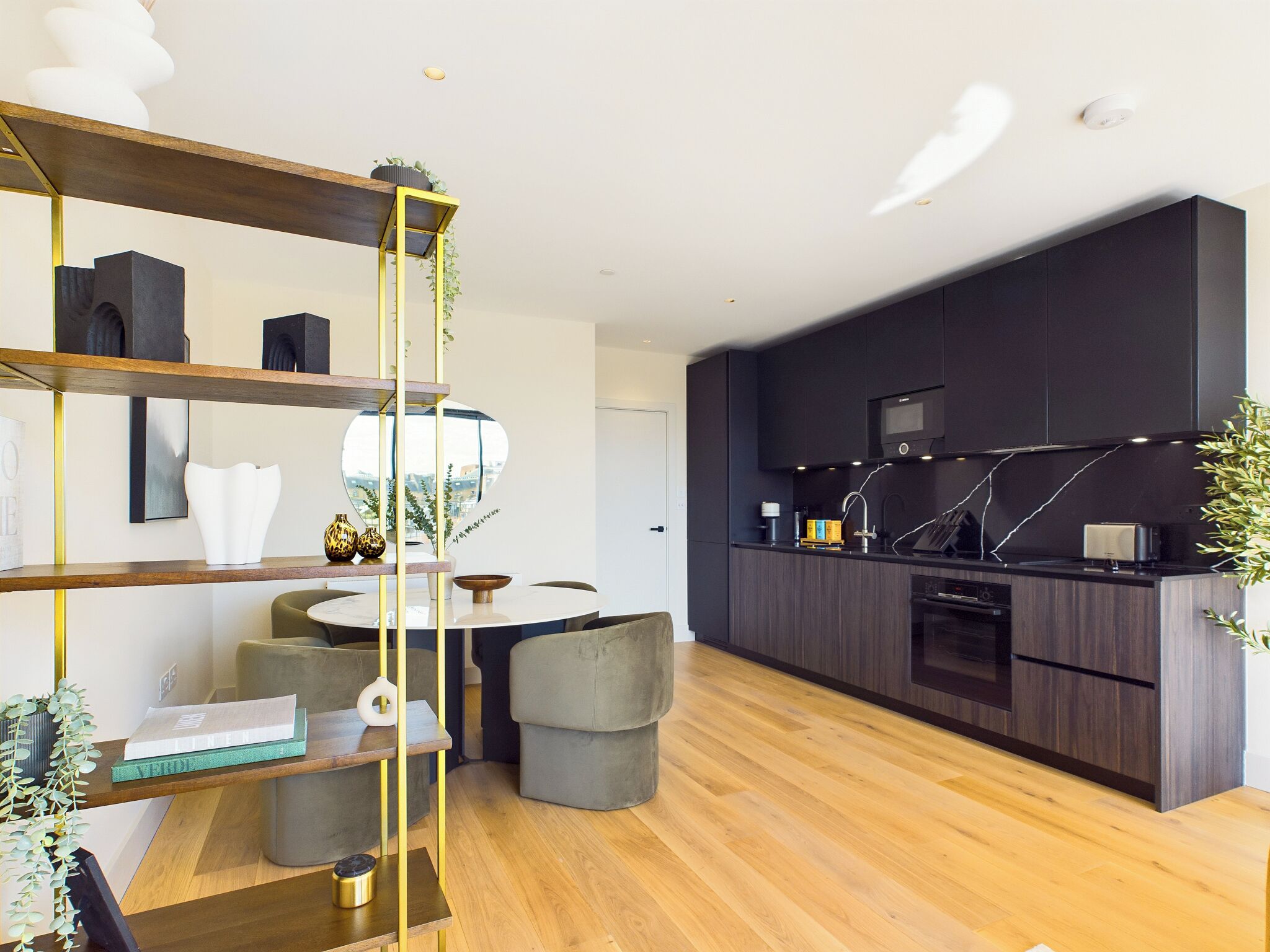 A modern kitchen with dark cabinetry, a central island, and a dining area with a round table and chairs.