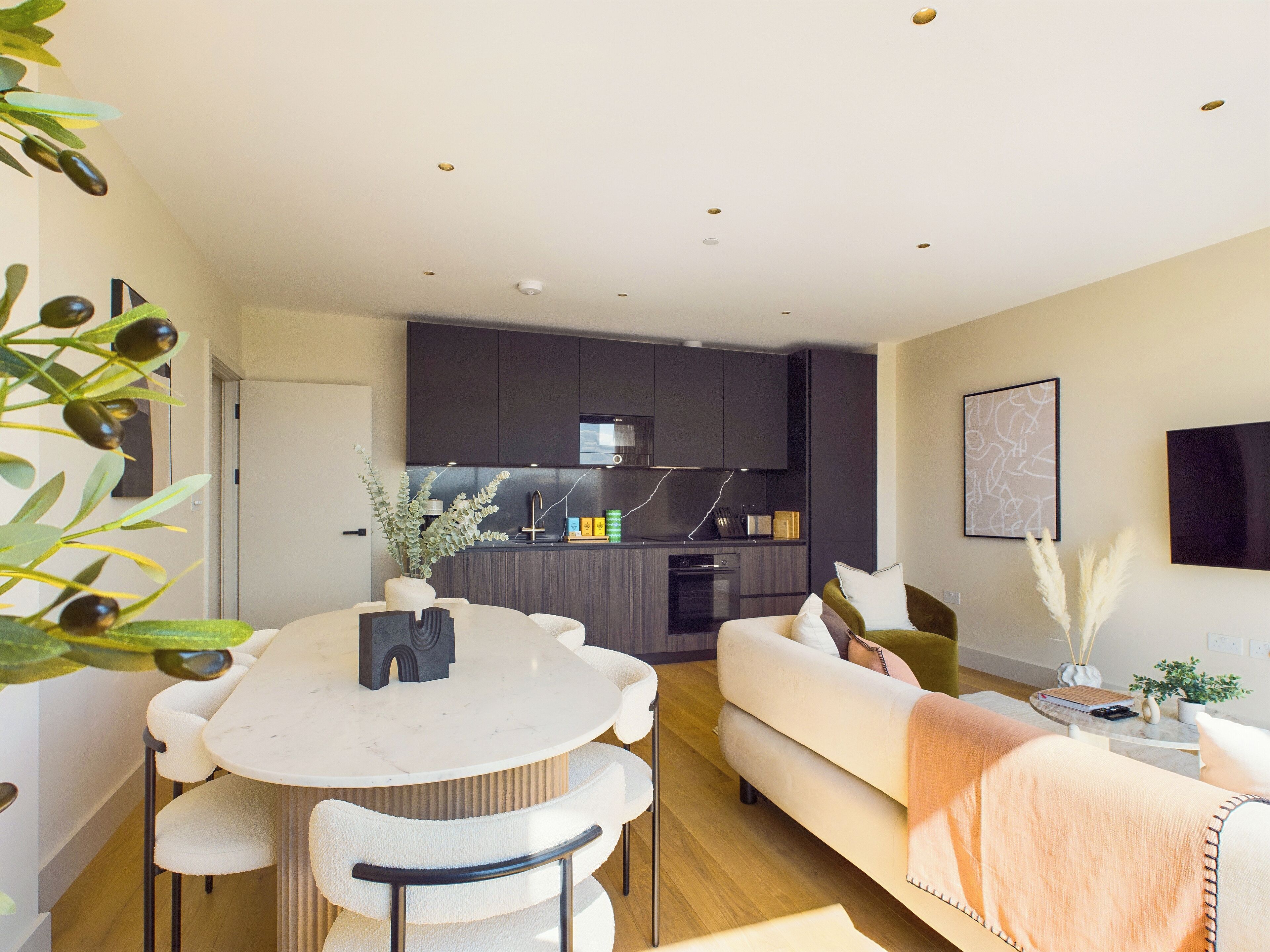 A modern living room with a round dining table, a sofa, and a kitchen in the background.