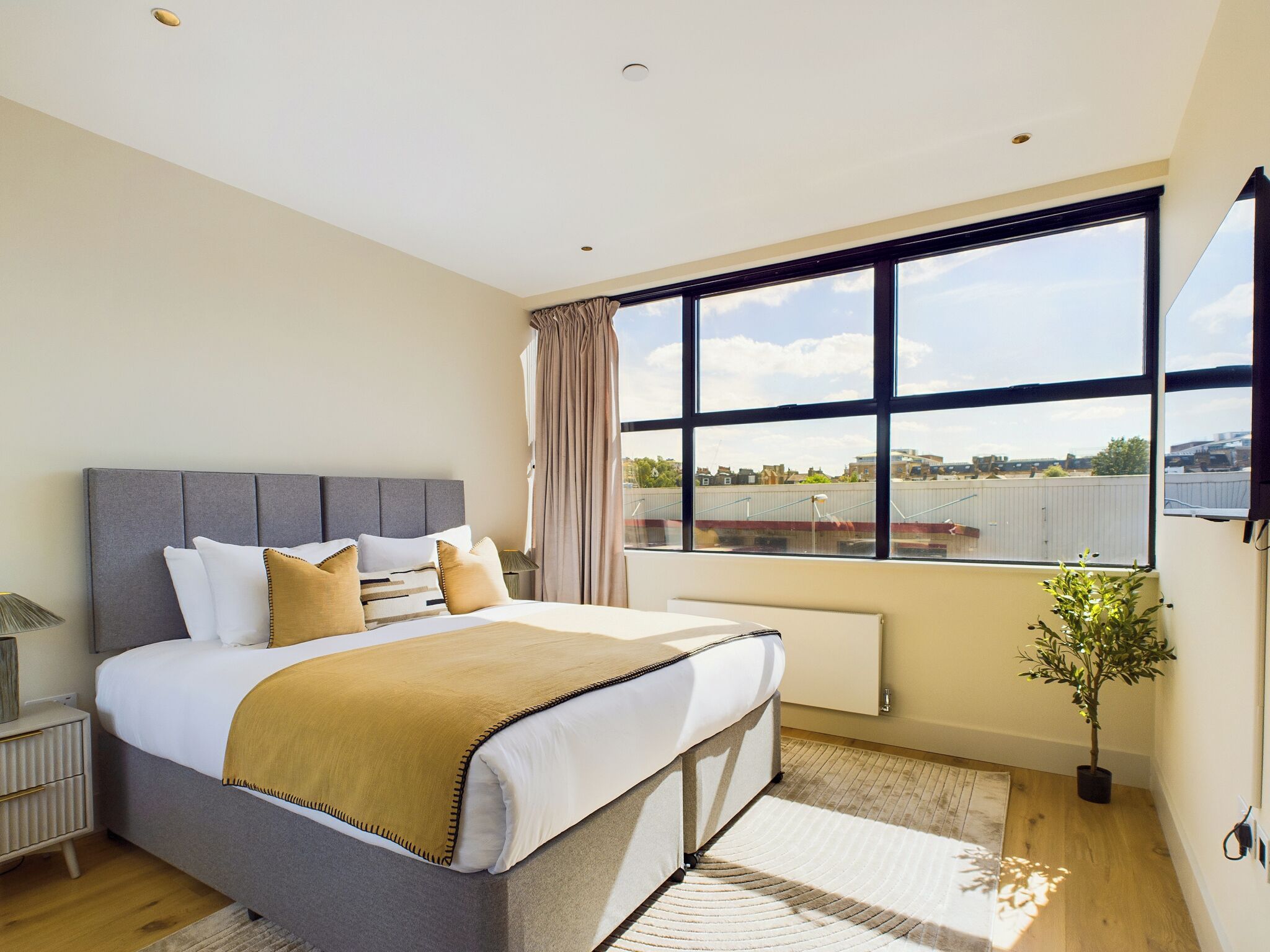 A modern bedroom with a large bed, a view of the city, and a potted plant.