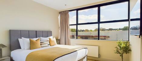 A modern bedroom with a large bed, a view of the city, and a potted plant.