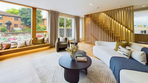 A modern living room with a large window, a sofa, a coffee table, and a staircase with a wooden railing. - Be London - The St Pancras Residences (London)