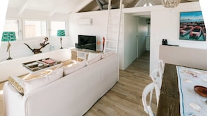 A modern living room with a white sofa, a TV, and a dining area with a table. - Seehütte Sonnenschilf (Rust)