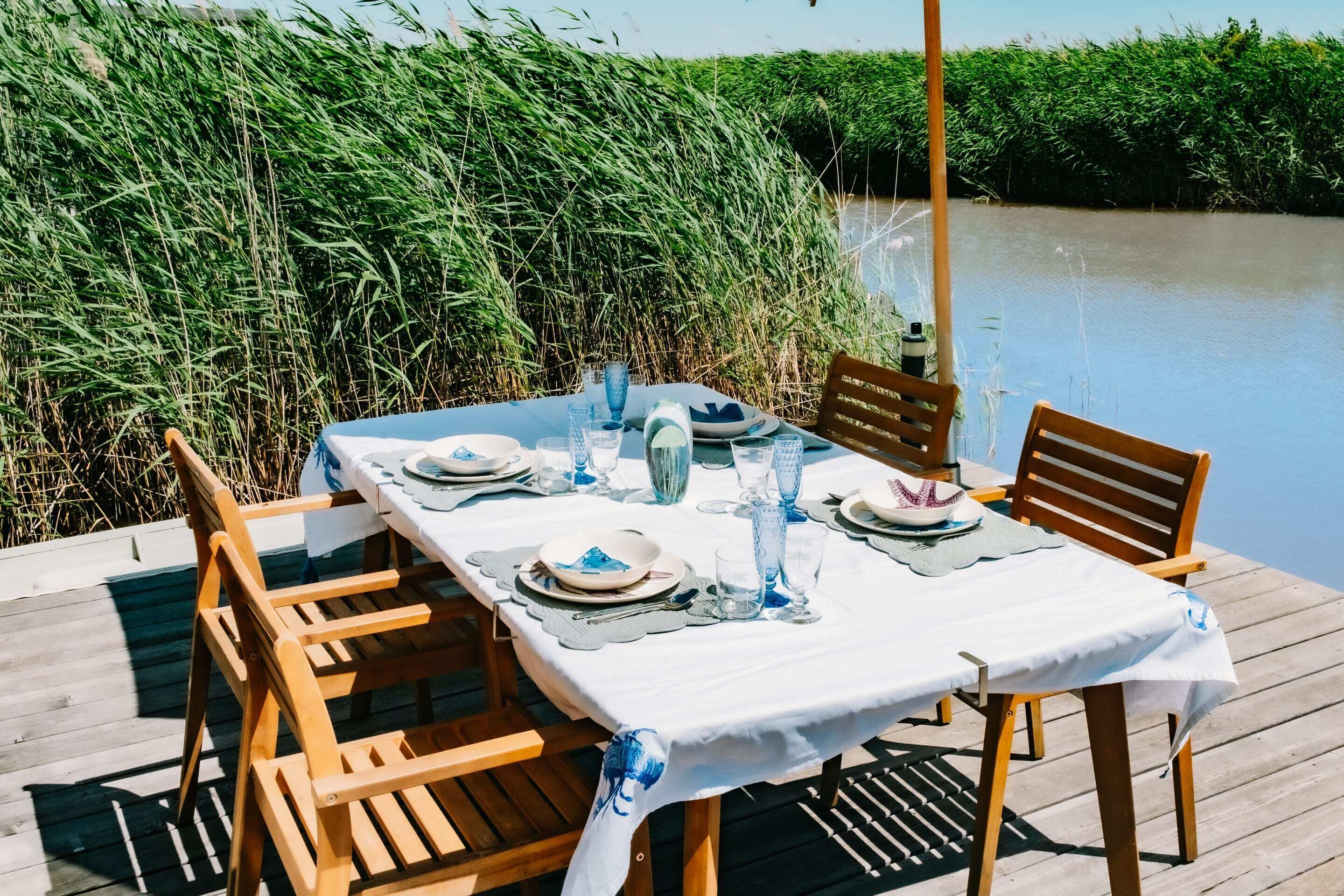 Een eettafel met stoelen op een houten terras, met uitzicht op een rivier.