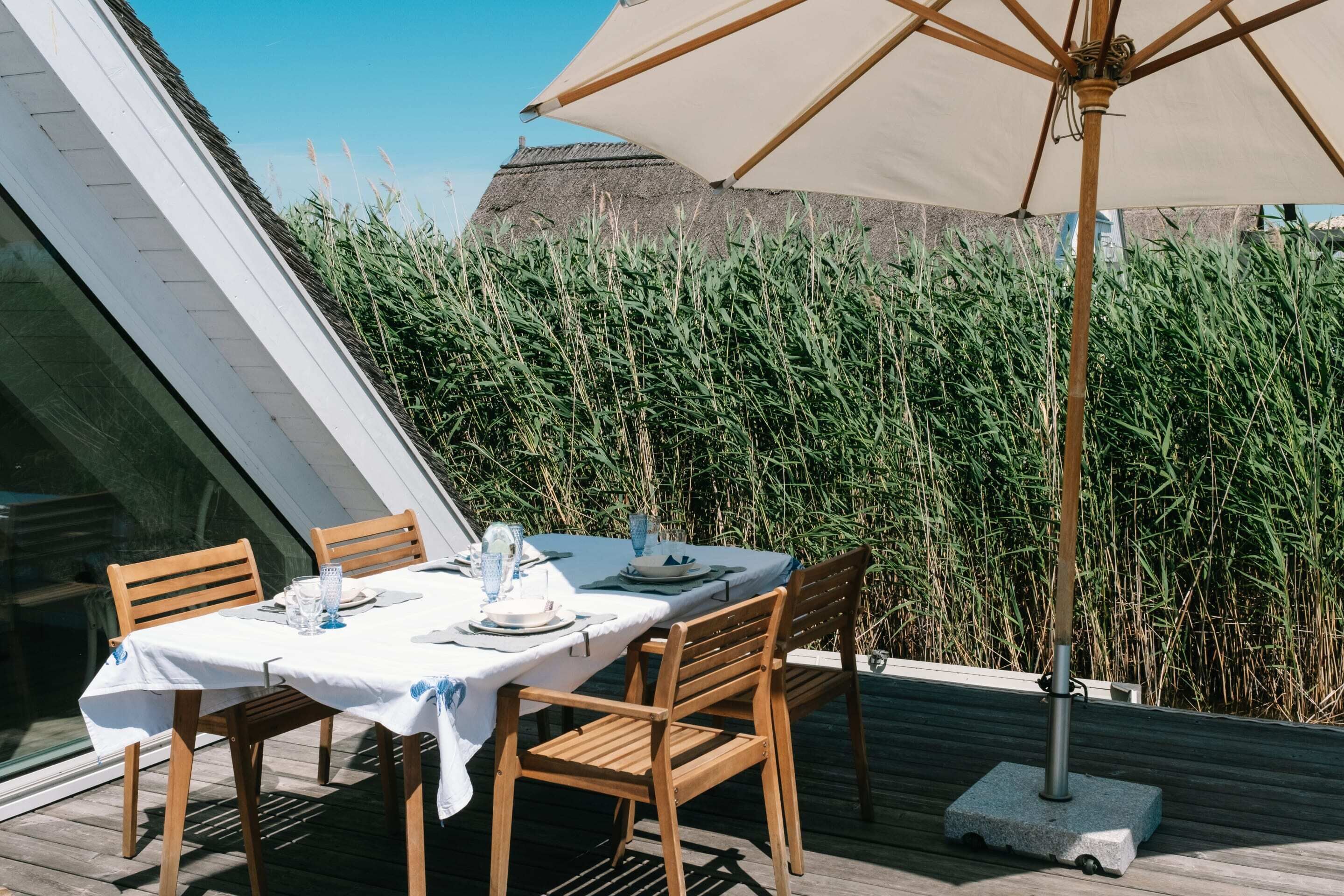 A dining area with a table set for four, surrounded by tall grasses, under a large umbrella.