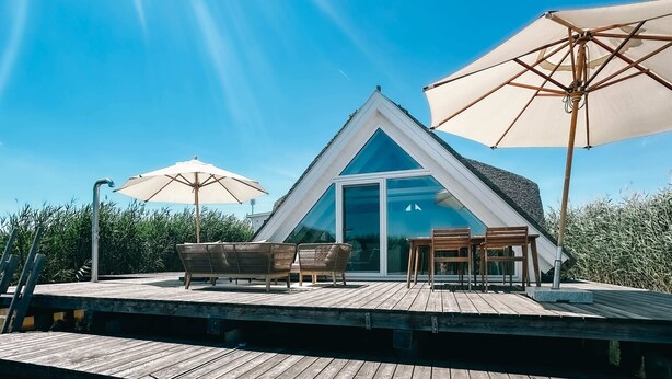 A modern villa with a triangular roof, a wooden deck, and outdoor seating. - Seehütte Sonnenschilf (Rust)