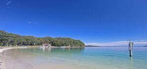A beach with clear water, a wooden pier, and a building on the shore.