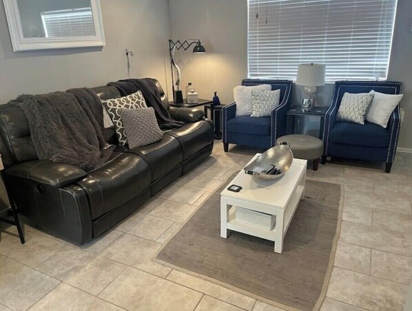 A living room with a black leather sofa, two blue armchairs, a white coffee table, and a lamp. - NEWLY RENOVATED HOME with high speed WiFi, gourmet kitchen, outdoor grilling. (Big Spring)