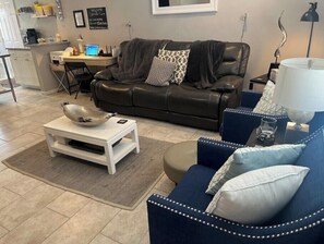 A modern living room with a black leather sofa, a blue armchair, and a white coffee table. There is a desk with a laptop and a computer monitor in the background. - NEWLY RENOVATED HOME with high speed WiFi, gourmet kitchen, outdoor grilling. (Big Spring)