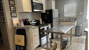 Una cocina con una mesa de acero inoxidable, estufa, microondas y refrigerador.